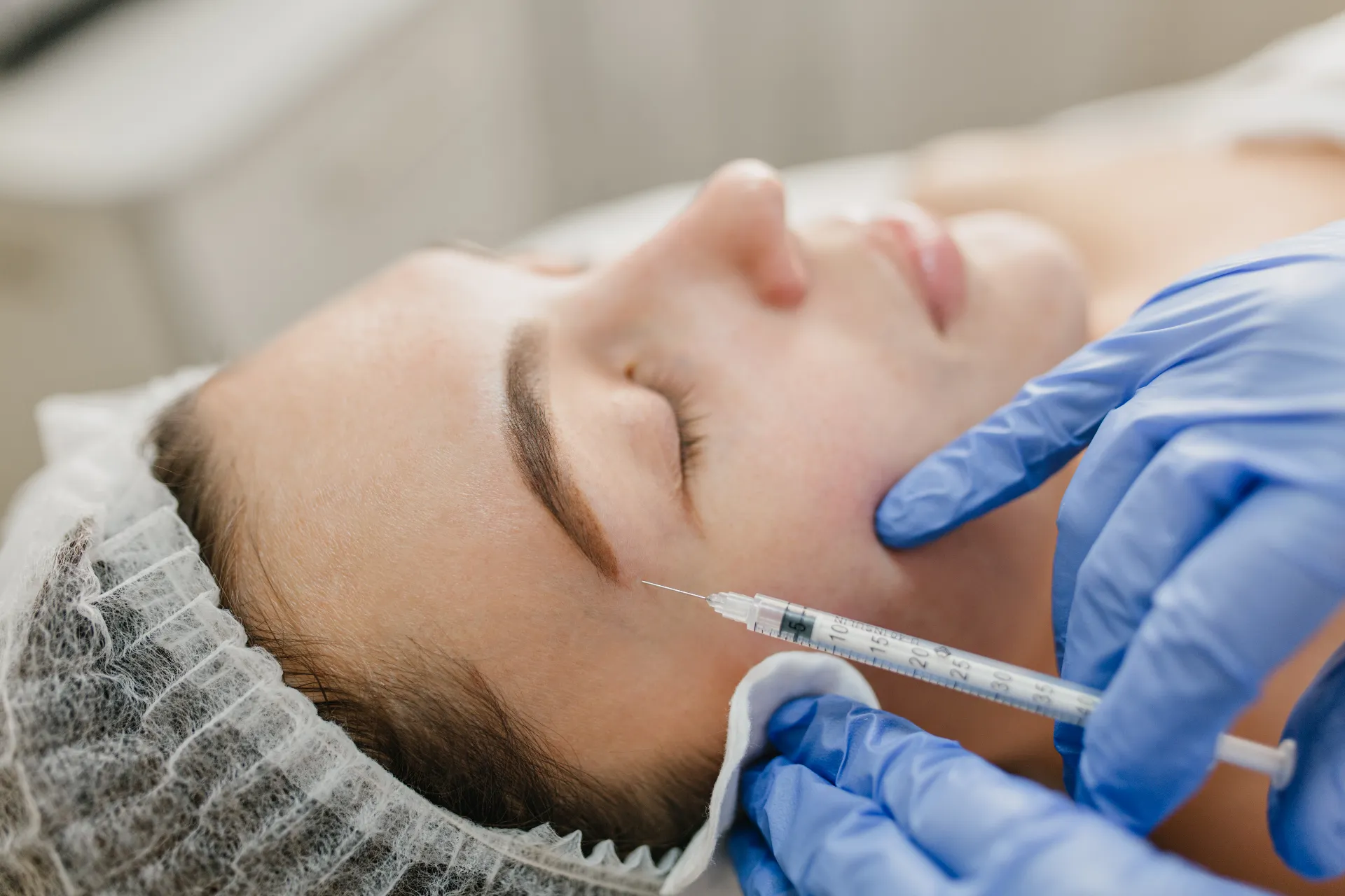 Close-up of a woman receiving a Botox injection in a clinic — professional dermatologist with blue gloves performing facial rejuvenation treatment for beauty and skincare.